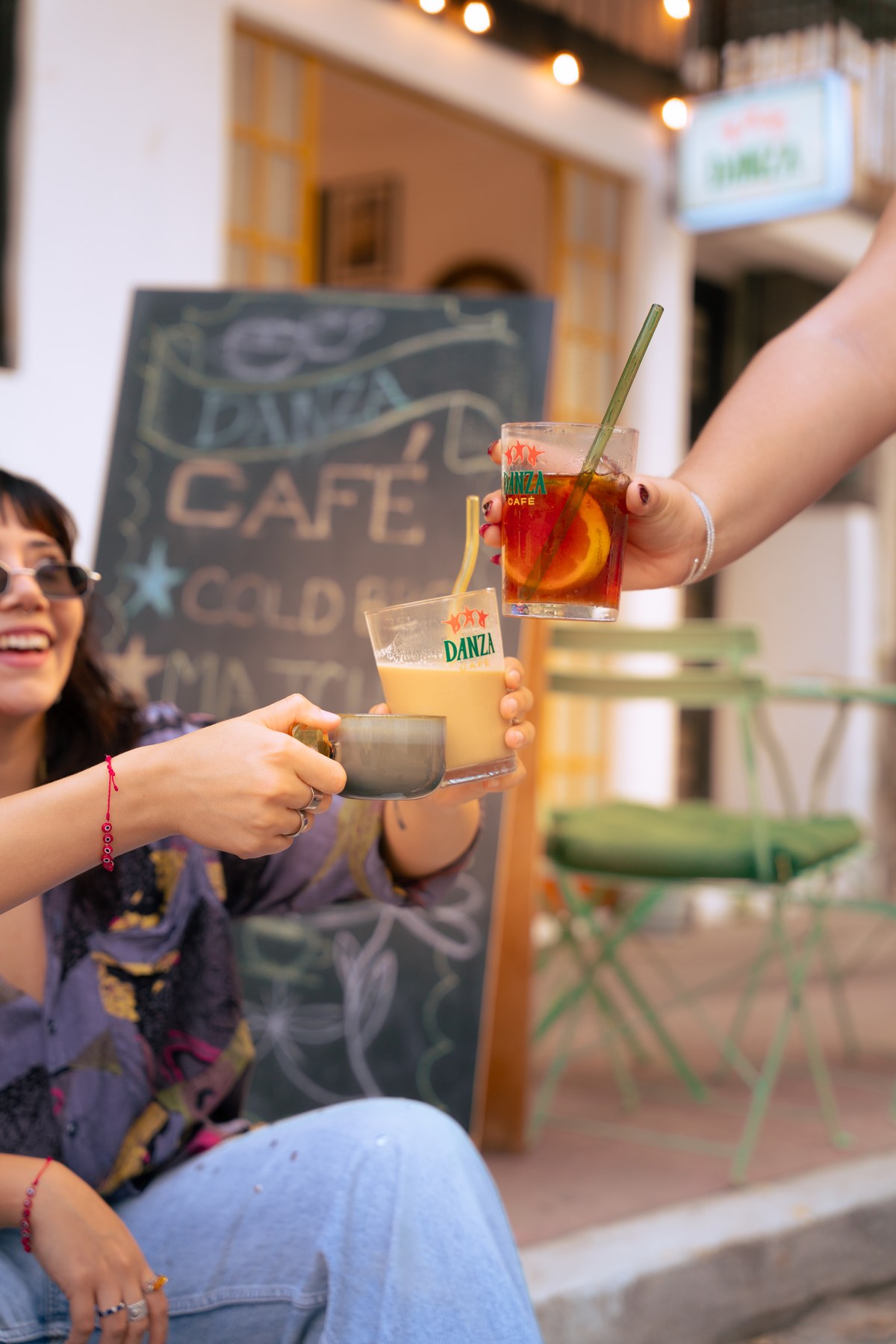 Three drinks raised in a toast outside Danza Café with chalkboard menu reading Cold Brew and Matcha
